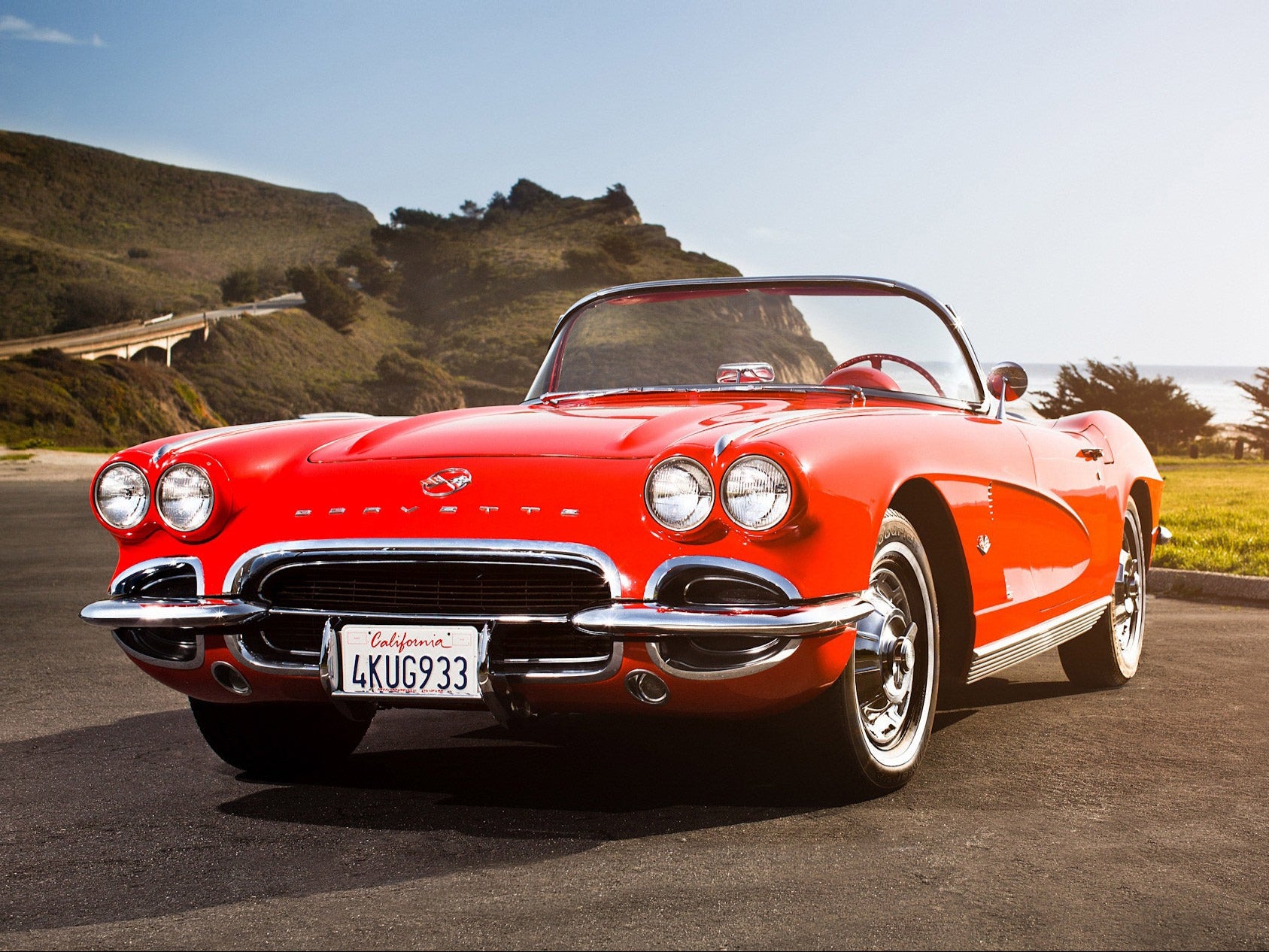 Red classic car on a road with a scenic background